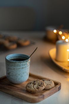Christmas background with Chocolate chip cookies, cup of tea. Cozy evening, mug of drink, holiday decorations, candles and lights garlands. Still life vertical photo