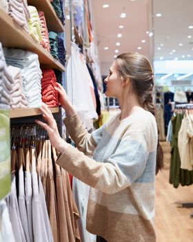 The girl chooses clothes in a large offline store, touches different things on the shelves. Concept of visiting mass events and public places where coronavirus is easily transmitted