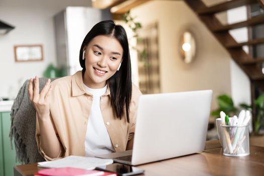 Smiling asian woman talks on video conference, working from home remotely with laptop, studying at online course or attending lecture.