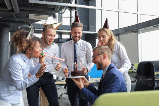 Happy business team with birthday cake are greeting colleague at office party.