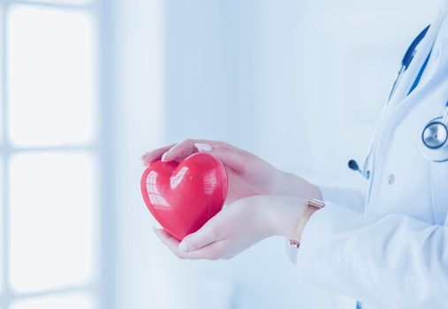 Female doctor with stethoscope holding heart, on light background.