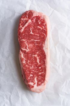 Big whole piece of raw beef meat, striploin on white parchment paper on craft background, zero waste packing. Steak without seasoning and salt. Top view, vertical