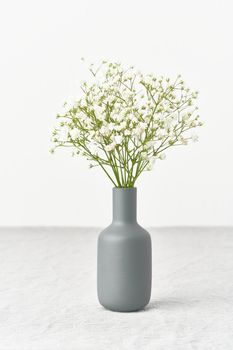 Gypsophila flowers in a vase. Soft light, Scandinavian minimalism, white walls, gray table. Empty space for text. Spring still life, vertical
