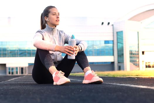 Beautiful young woman in sports clothing drinking water after sport exercise outdoors in stadium.