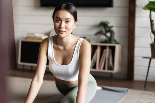 Asian girl doing yoga stretching at home, workout in her living room, wearing activewear.