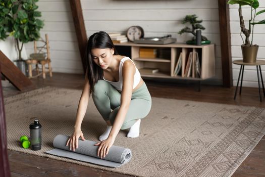 Asian fitness girl finish training,workout at home, rolling floor mat after exercises in living room.