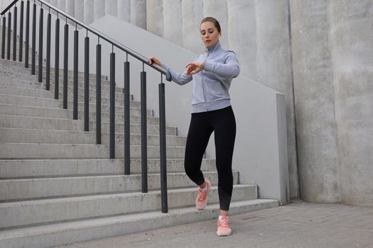 Attractive young fitness woman looking at her smartwatch while standing near the stairs outdoors.
