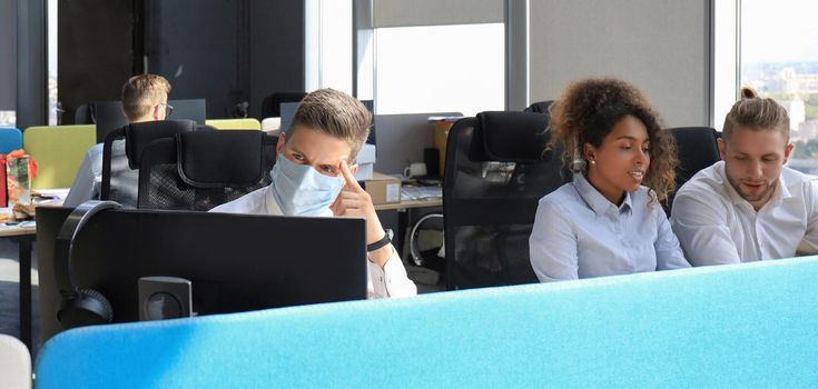 Businessman is working in preventive medical mask in the epidemic in office, collegues at the background