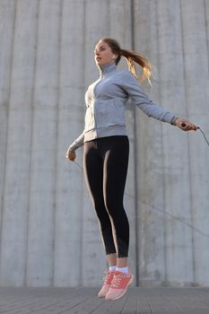 Portrait of fit young woman with jump rope outdoors. Fitness female doing skipping workout outdoors on sunrise or sunset.