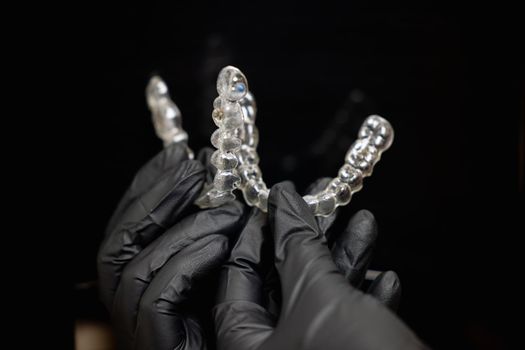 Close-up shot of doctors hands in black gloves holding silicone mouth guard. Teeth care. High quality photo