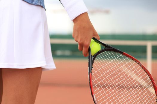 Close up of woman is holding tennis racket on hard tennis court. Tennis ball in player hand