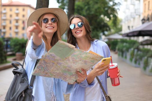Two pretty girls dressed in summer clothes holding city map while standing outdoors