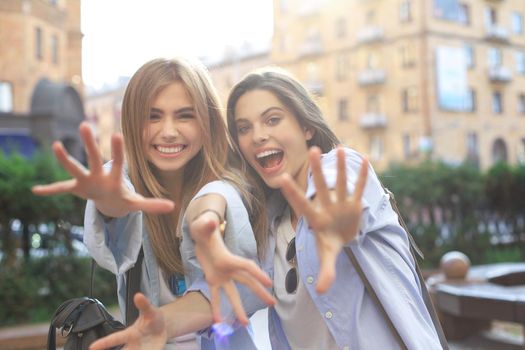 Two young smiling hipster women in summer clothes posing on street.Female showing positive face emotions