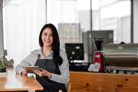 Cheerful young asian woman owner holding digital tablet while standing in her cafe, young entrepreneur conceptual.