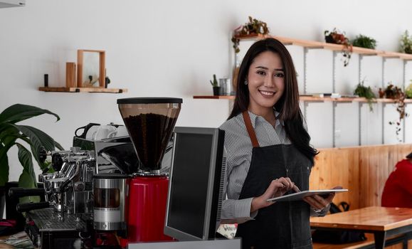 Cheerful young asian woman owner holding digital tablet while standing in her cafe, young entrepreneur conceptual.