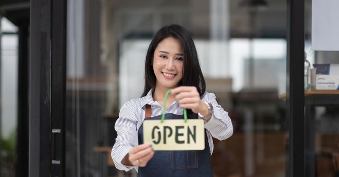 Startup successful small business owner sme beauty girl stand hand hold open sign coffee shop or restaurant. Portrait of young asian woman barista cafe owner. SME entrepreneur business concept