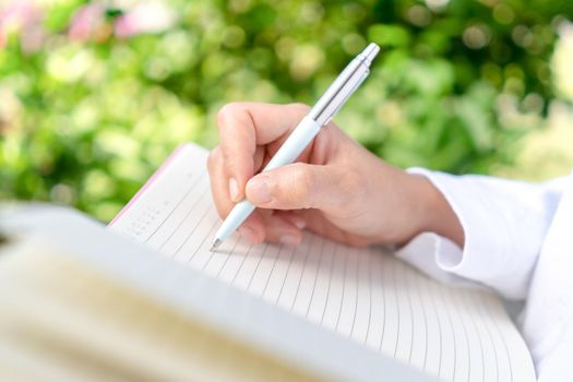 Woman hand writing down in small white memo notebook for take a note not to forget or to do list plan for future. 