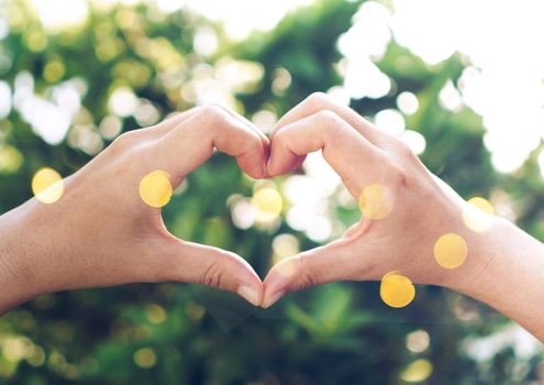 Woman hand do heart shape on green nature bokeh tropical background.