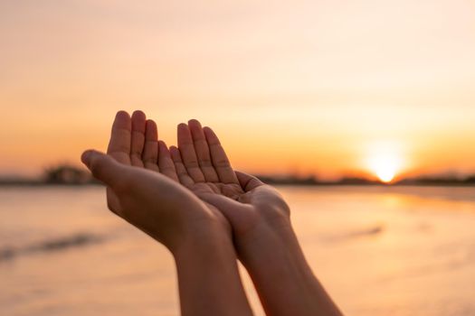 Woman hands place together like praying from nature in front of sunset beach background.