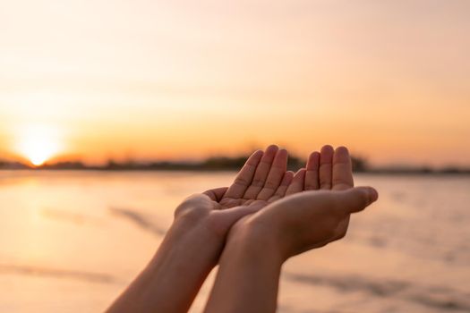 Woman hands place together like praying from nature in front of sunset beach background.