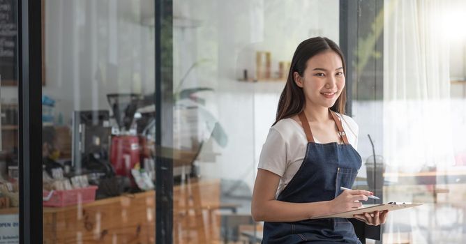 Cheerful smiling young Asian woman entrepreneur at coffee shop counter with order list.