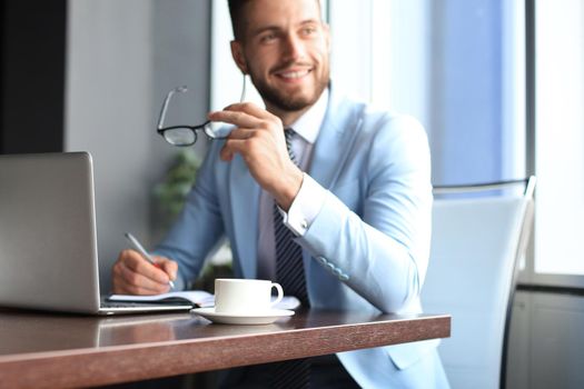 Portrait of happy businessman sitting at office desk, smiling.