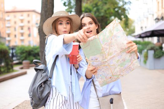 Two pretty girls dressed in summer clothes holding city map while standing outdoors