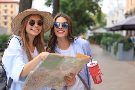 Two pretty girls dressed in summer clothes holding city map while standing outdoors