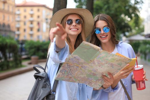 Two pretty girls dressed in summer clothes holding city map while standing outdoors