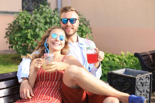 Romantic young couple in summer clothes smiling and taking selfie while sitting on bench in city street.