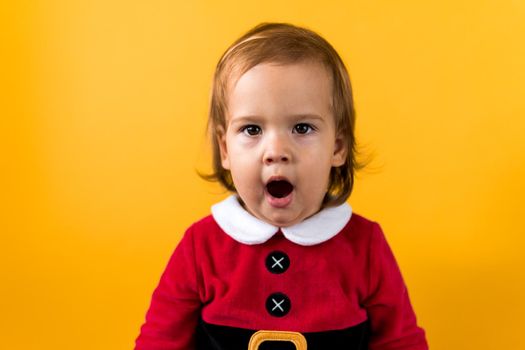 Portraite Emotion Cute Happy Cheerful Chubby Baby Girl in Santa Suit Yawns As If Singing At Orange Background. Child Christmas Scene Celebrating Birthday. Kid Have Fun Spend New Year Time Copy Space.