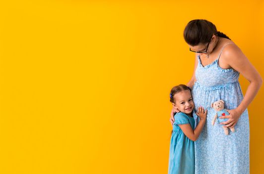 Motherhood, love, Childhood, pregnancy, hot summer - Banner pregnant unrecognizable mother woman expecting baby blue dress lillte Daughter girl sibling teddy bear hug mum belly on yellow background.