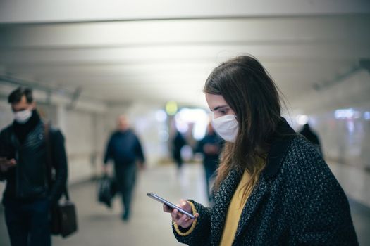 young woman in a protective mask reading a text message at a metro station. coronavirus in the city