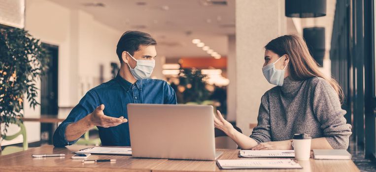 close up. business colleagues in protective masks sitting at the office Desk.