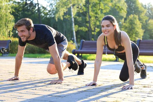 Young couple doing exercise together while working out outdoors in park