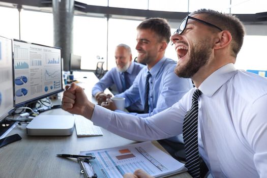 Group of modern business men in formalwear smiling and gesturing while working in the office