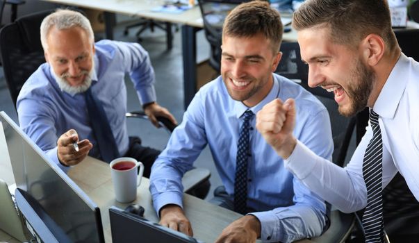 Group of modern business men in formalwear smiling and gesturing while working in the office