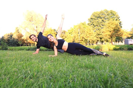 Young couple doing exercise together while working out outdoors in park