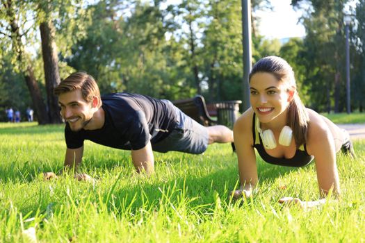 Young sports woman and man doing plank exercise together outdoors in urban park