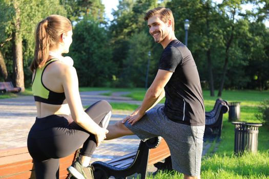 Young couple stretching their legs together while working out at park outdoors