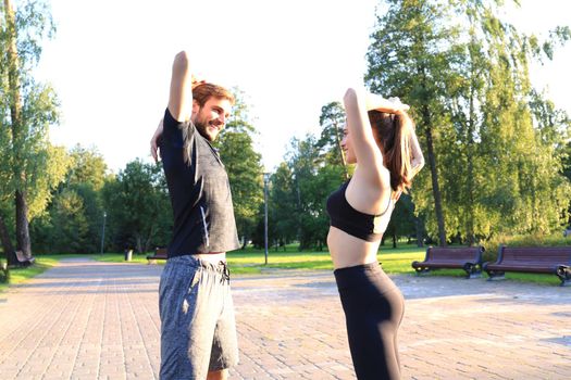 Attractive couple doing stretch together and smiling while working out in park outdoors