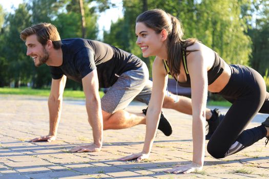 Young couple doing exercise together while working out outdoors in park