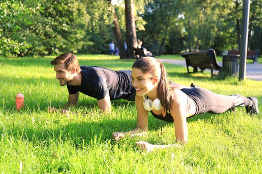 Young sports woman and man doing plank exercise together outdoors in urban park