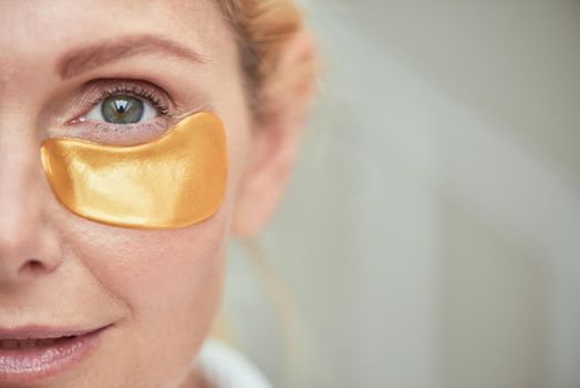 Under eye patch on smiling middle aged caucasian woman face, selective focus. Beauty, skincare and cosmetology concept