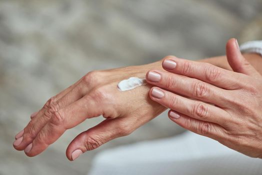 Close up of beautiful female hands applying white cream on light background. Beauty, skincare and cosmetology concept