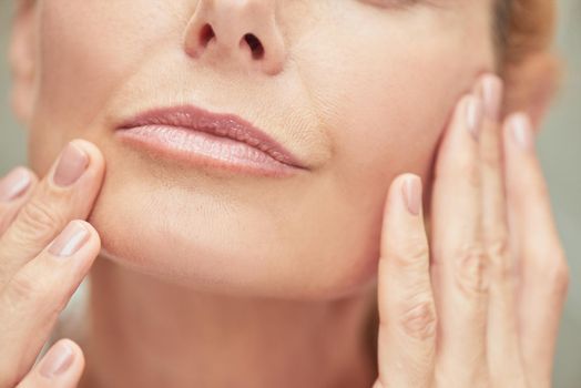 Well-groomed lips of middle aged caucasian woman with manicured fingers near face, cropped. Beauty, skincare and cosmetology concept