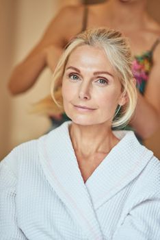 Portrait of beautiful middle aged caucasian woman at spa resort with cosmetologist on background. Beauty, skincare and cosmetology concept