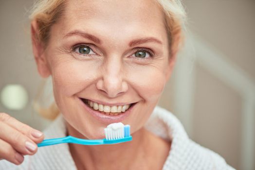 Portrait of happy middle aged caucasian woman with toothbrush in hand looking at camera and smiling. Beauty, skincare and cosmetology concept