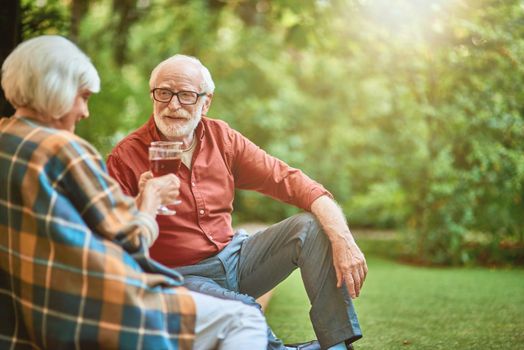 Happy senior man looking at his wife while holding glasses with red wine outdoors. Relationship and family concept. Copy space