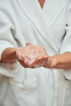 Woman in white bathrobe washing hands with soap foam, cropped. Beauty, skincare and cosmetology concept